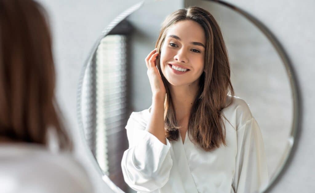 Woman smiles in mirror, admiring the condition of her skin.